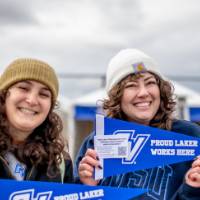 Two alums smiling holding GV Laker pennants